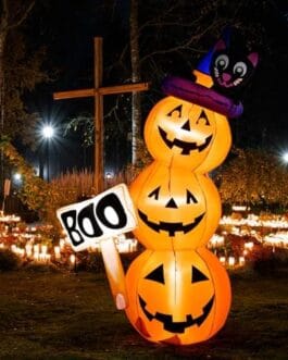 Décoration d’Halloween avec un monstre chauve-souris noir sur un totem de citrouilles lumineuses et torches en feu dans un parc nocturne.